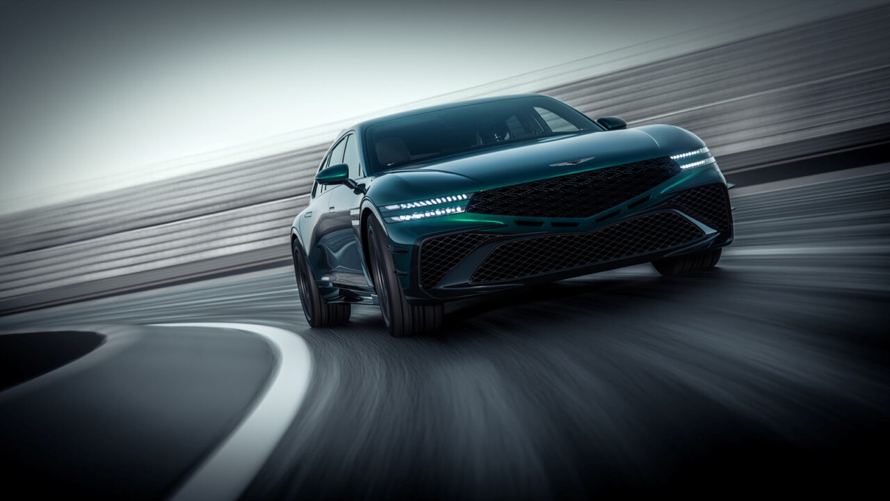 매끄러운 짙은 녹색의 스포츠 세단이 곡선형 레이싱 트랙을 빠르게 달리고 있으며, 낮은 전면 각도에서 촬영되었습니다. 차량의 LED 헤드라이트에 조명이 켜지고 배경은 모션 블러 처리되어 차량의 속도를 강조합니다.