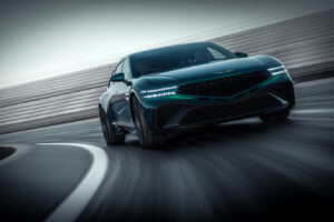 매끄러운 짙은 녹색의 스포츠 세단이 곡선형 레이싱 트랙을 빠르게 달리고 있으며, 낮은 전면 각도에서 촬영되었습니다. 차량의 LED 헤드라이트에 조명이 켜지고 배경은 모션 블러 처리되어 차량의 속도를 강조합니다.